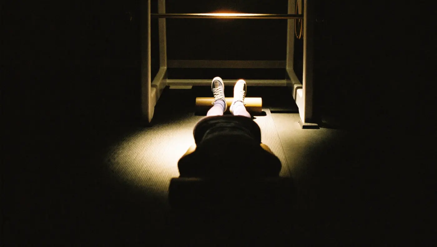 A member lying back on a mat beside a foam roller in the recovery corner, lit by a single warm lamp